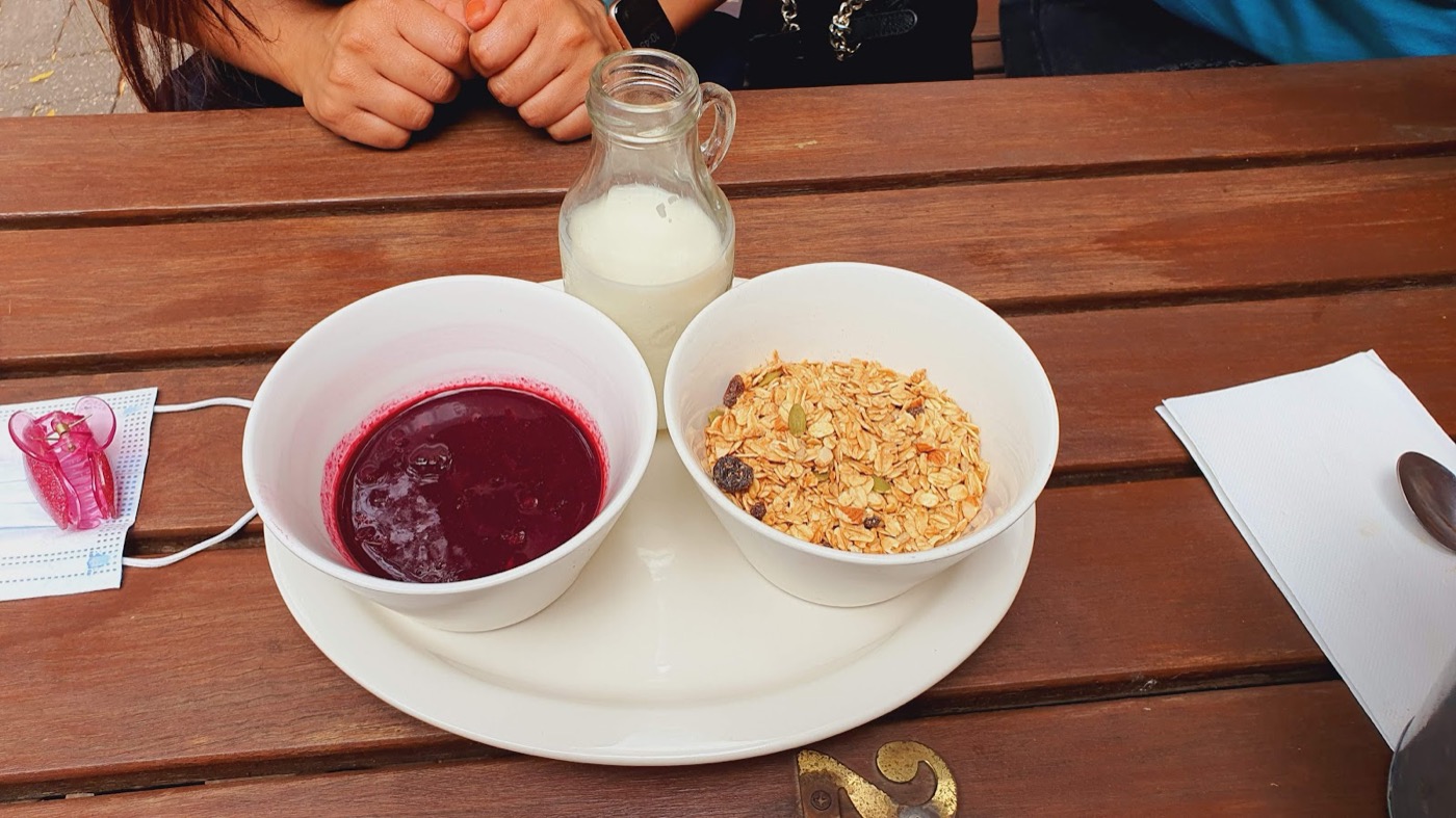 Two white bowls on a timber table, one with berry compote and one with granola, next to a small bottle of milk
