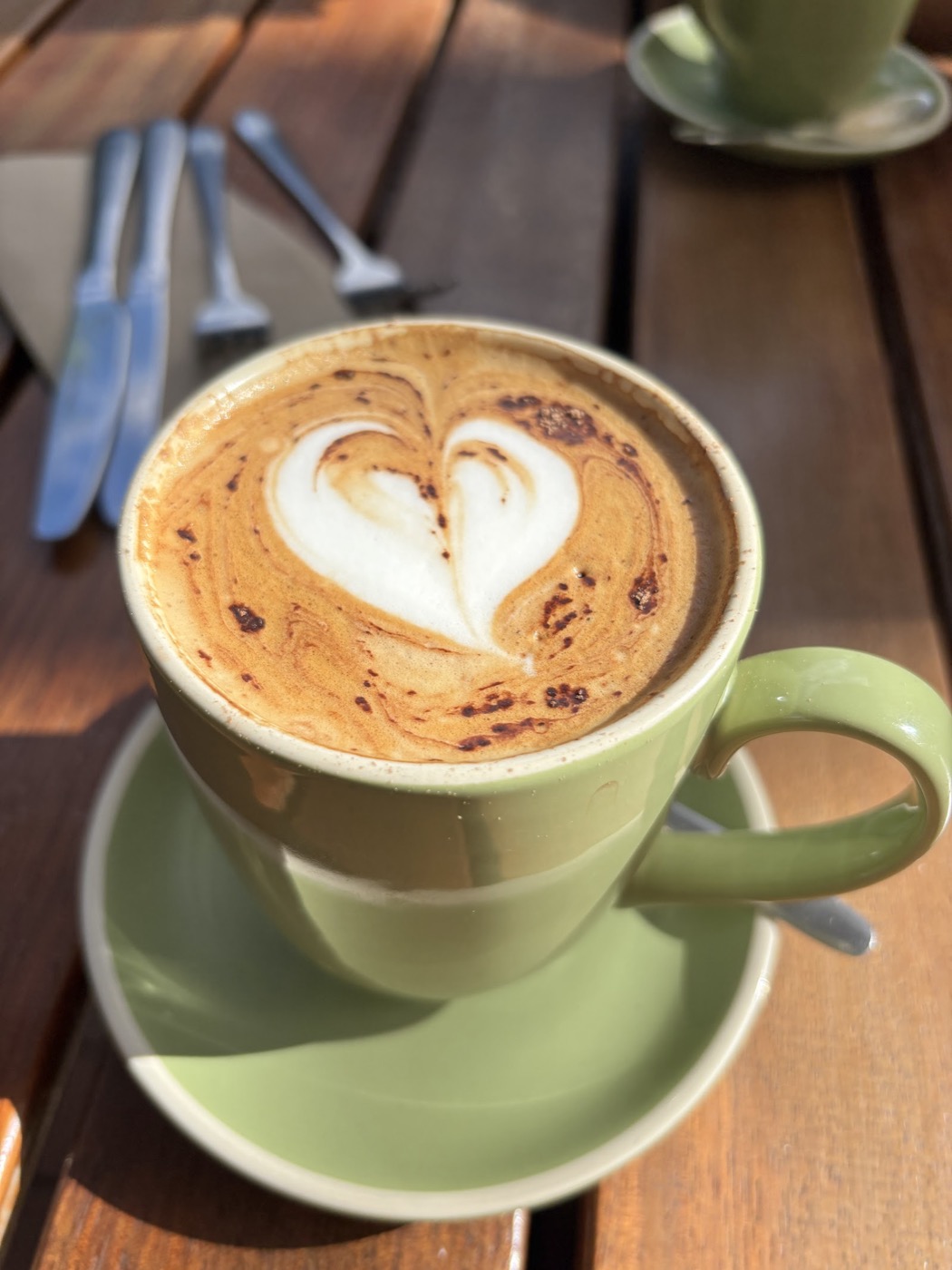 A latte with a heart pattern in the foam, in a green cup on a green saucer, on a timber table