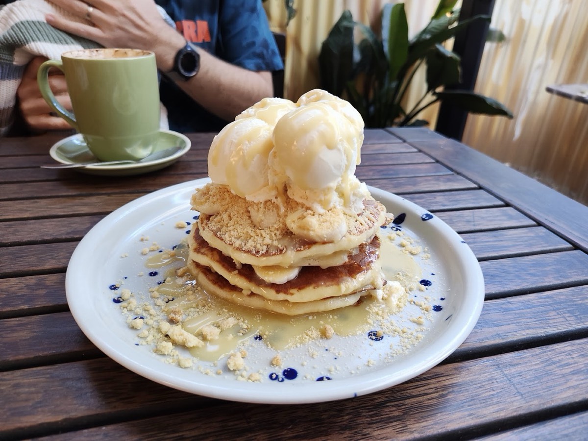 A tall stack of pancakes topped with scoops of ice cream on a white plate, with a green coffee cup beside it