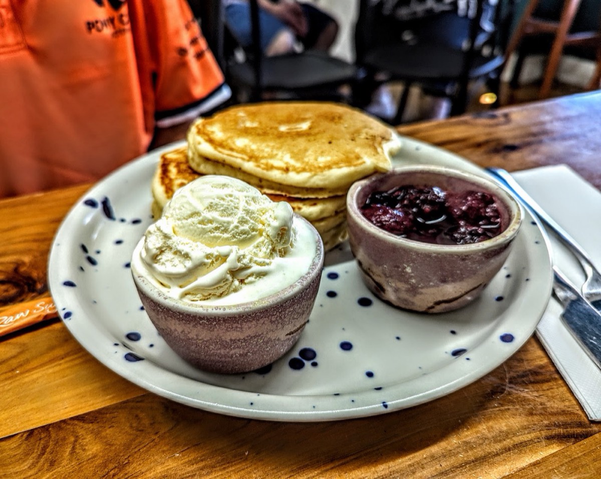 Pancakes on a speckled plate with a pot of whipped cream and a pot of berry compote